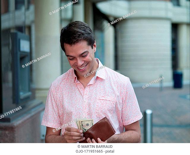 Smiling man holding pocket near ATM machine