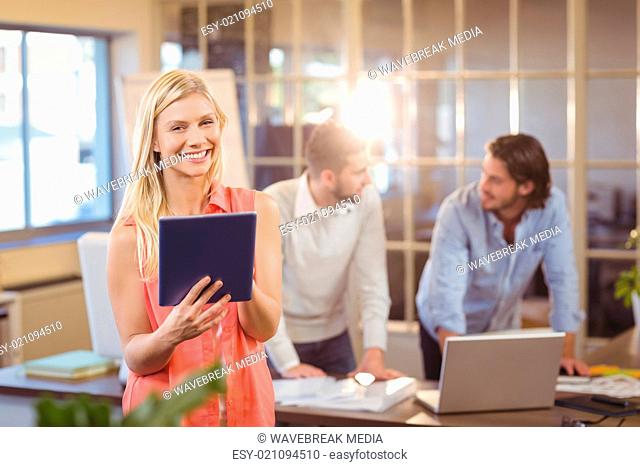 Smiling businesswoman using digital PC with male colleagues working