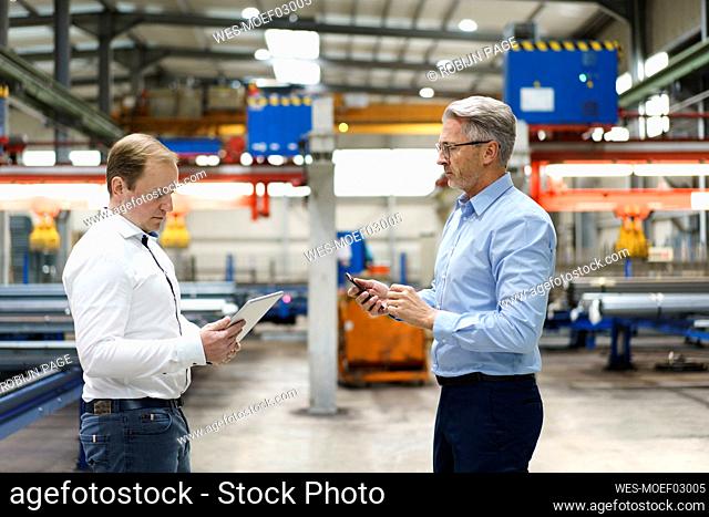 Two businessmen with tablet and mobile pohone having a meeting in a factory