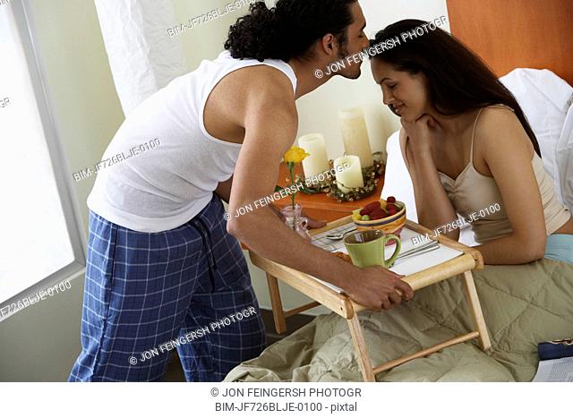 Man kissing woman as he serves her breakfast in bed