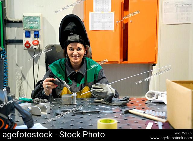 A woman employed in a modern factory for the production and processing of metals in a work uniform welds metal materials. High quality photo