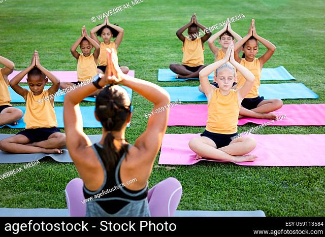 Female teacher and group of diverse students practicing yoga and meditating in the garden at school
