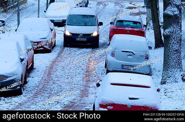 28 November 2023, Berlin: Snow lies on cars in the capital in the early morning, while a van drives over a slippery road with cobblestones