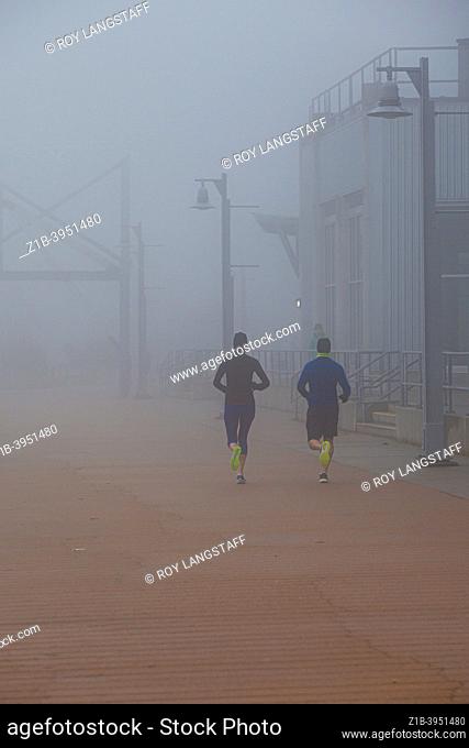 Two people running in fog along the Steveston waterfront British Columbia Canada