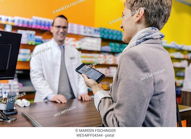 Smiling woman with cell phone at counter in pharmacy