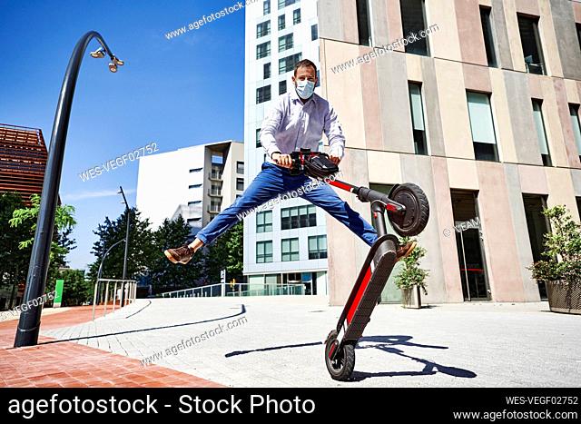 Entrepreneur jumping while holding electric push scooter in city during sunny day