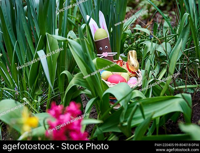 PRODUCTION - 01 April 2022, Berlin: ILLUSTRATION - An Easter nest with made bunny, chocolate bunny, colored eggs and chocolate eggs lie in a flower bed