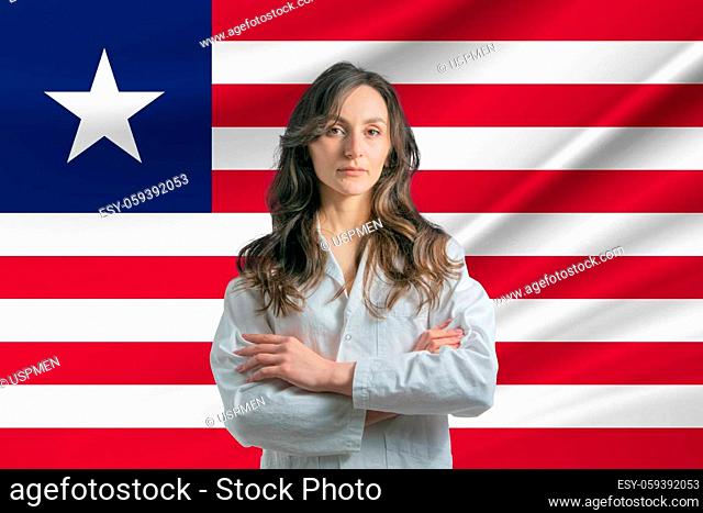 Medicine in Liberia. Happy beautiful female doctor in medical coat standing with crossed arms against the background of the flag of Liberia