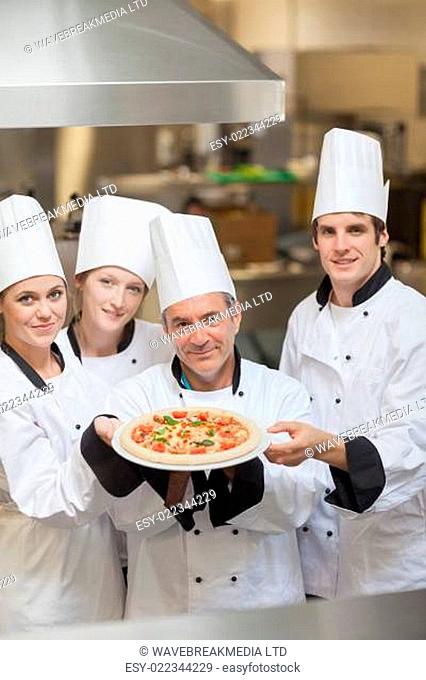 Four Chef's holding a pizza while smiling