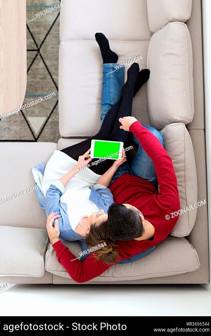 Young couple relaxing at home using tablet computers reading in the living room on the sofa couch