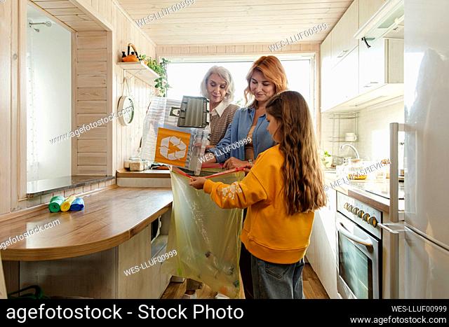 Grandmother, mother and daughter sorting recycling waste in kitchen