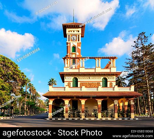 Facade of the clock tower in Montaza public park with decorated stone wall, green wooden window shutters, and red tile canopies after sunrise, Alexandria, Egypt