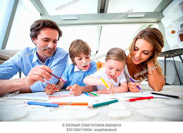 Charming family with children drawing together on the floor in a living room
