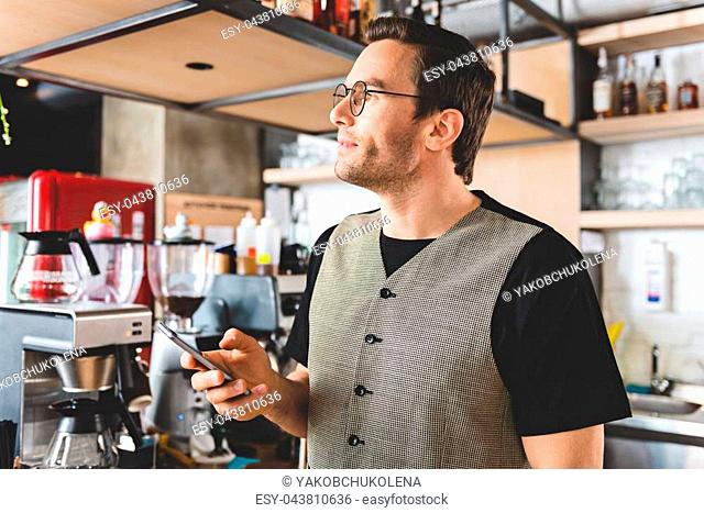 Side view stubbled man expressing thoughtfulness while sending sms by cellphone in comfortable confectionary shop