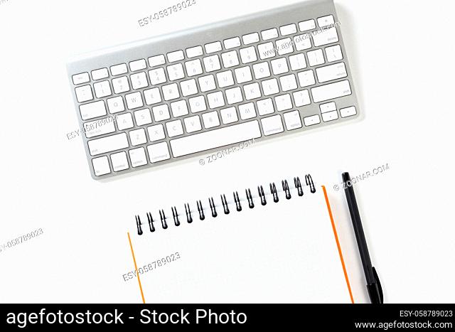 Top view of businessman workplace. Spiral notepad, pen and computer keyboard on white surface. Education, creativity and working concept with copy space