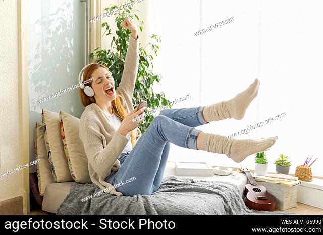 Carefree young woman listening to music with headphones at home