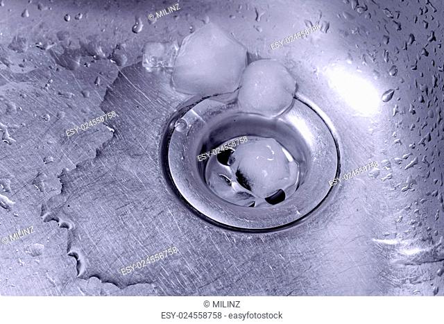 Metallic Kitchen sink with melting ice and water drops in blue duotone shot from low angle