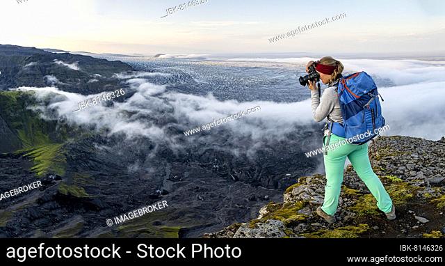 Hiker photographs spectacular landscape, fog on cliffs and glacier Myrdalsjökull, Pakgil, Iceland, Europe