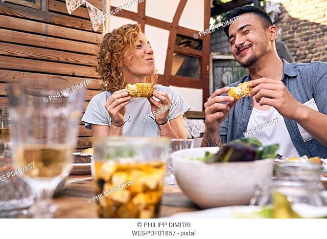 Couple eating grilled corn cobs at a backyard barbecue