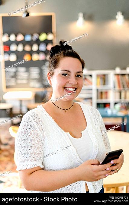 Happy voluptuous woman using mobile phone while standing in coffee shop