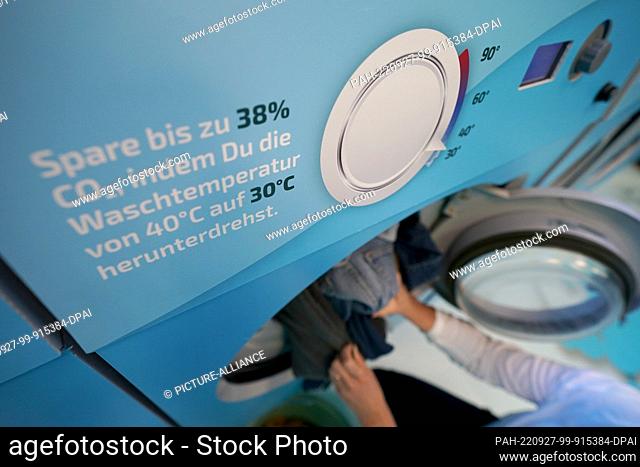 27 September 2022, Hamburg: A woman fills a washing machine during the Cold Laundromat campaign in the Winterhude district
