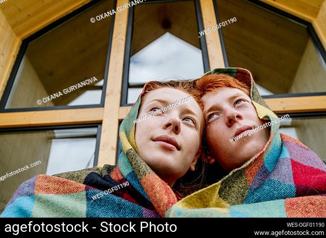 Thoughtful woman with boyfriend wrapped in blanket
