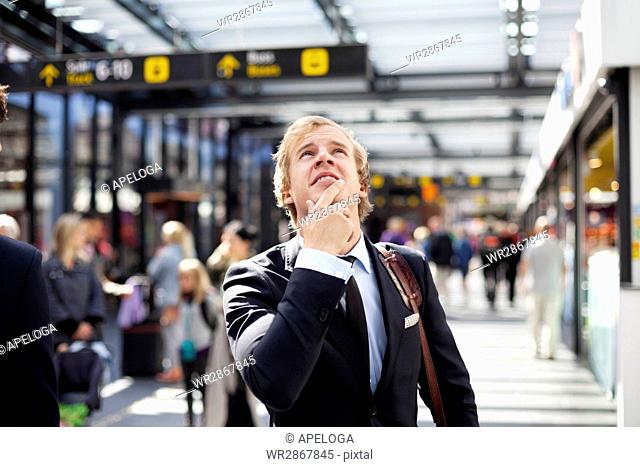 Young businessman looking up while standing at railroad station