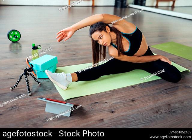 Beautiful young woman practicing yoga, is engaged with the teacher online via a tablet. Home sports concept