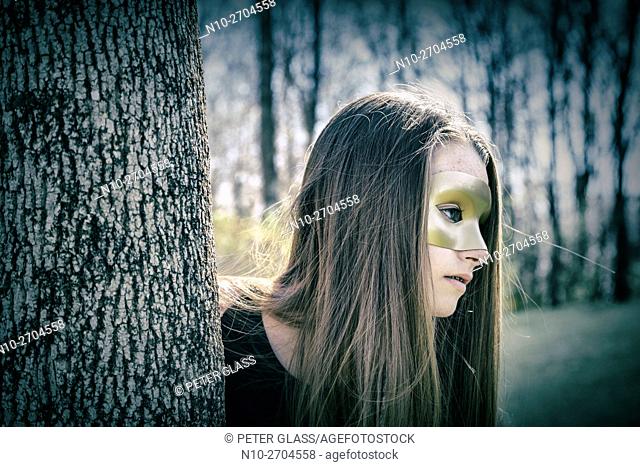 Teenage girl wearing a mask and standing behind a tree