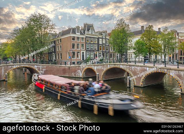 Netherlands. Summer sunset on the canals of Amsterdam. Pleasure boat floats between the bridges. Traditional houses and bicycles on the waterfront