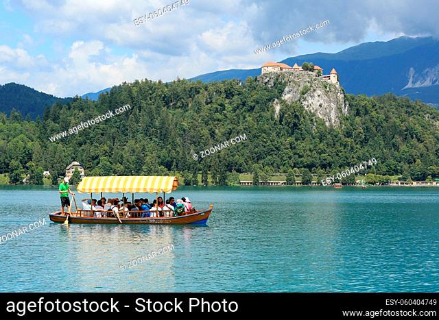 SLOVENIA, BLED - JULY 15, 2019: Traditional turist boat. Beautiful mountain lake in summer with castle on cliff and alps in the background