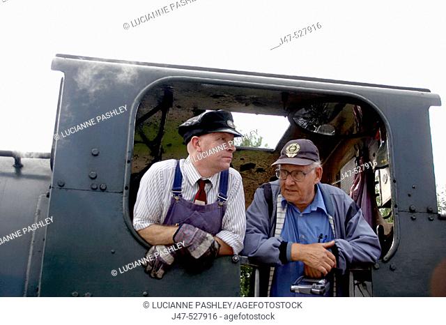 2, train drivers leaning out of the window of their steam train