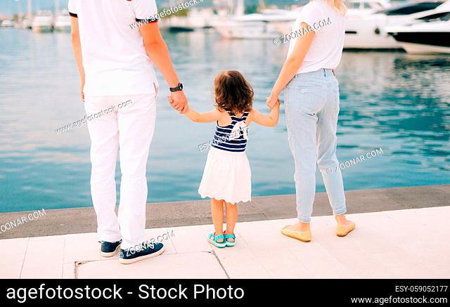 Parents with a daughter at the sea. Dad and mom are holding the baby by the hand