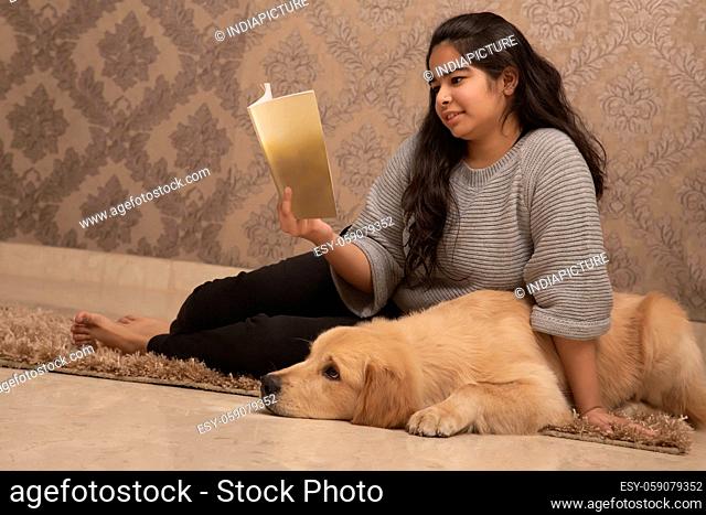 A YOUNG GIRL SITTING WITH PET DOG AND READING BOOK