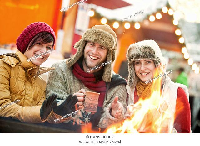 Austria, Salzburg, Man and women by fire at christmas market, smiling