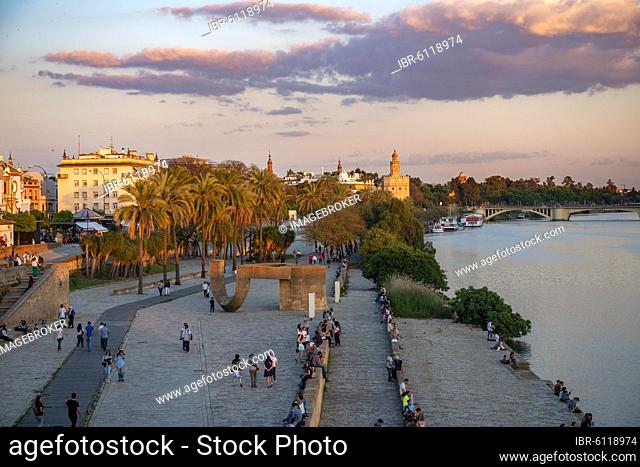 Waterfront promenade Muelle de la sal at the river Rio Guadalquivir with Monumento a la Tolerancia and Torre del Oro, sunset, Sevilla, Andalusia, Spain, Europe