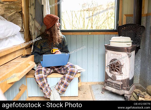 Thoughtful young man using laptop in tiny cabin rental