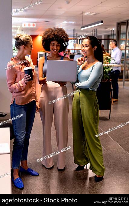 Smiling biracial female advisors discussing over laptop while working together at modern workplace