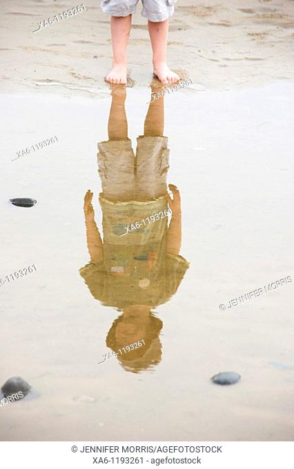 A boy's legs and his reflection in a puddle on the beach