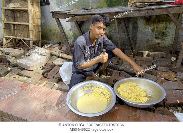 a young man crush corn in a metallic bowl. dhaka. bangladesh. asia