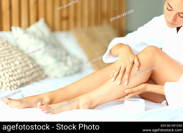 Close up of a woman applying moisturizer cream on legs sitting on the bed