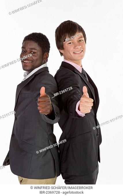 Two young businessmen standing back to back and making a thumbs-up gesture