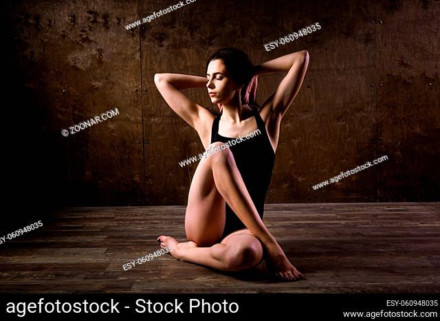 beautiful young girl dancer with long flowing hair in black clothes, a gymnastic swimsuit, in a dance pose on a wooden floor with a dark background