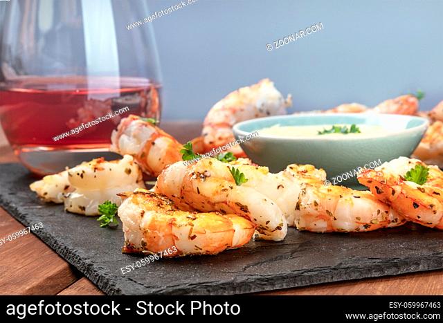 A closeup photo of plate of cooked shrimps with a sauce and a glass of wine, with copy space
