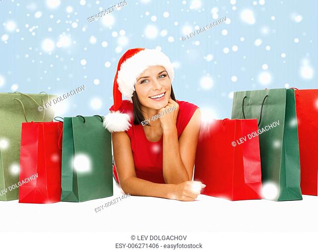 sale, gifts, christmas, x-mas concept - smiling woman in red shirt and santa helper hat with shopping bags