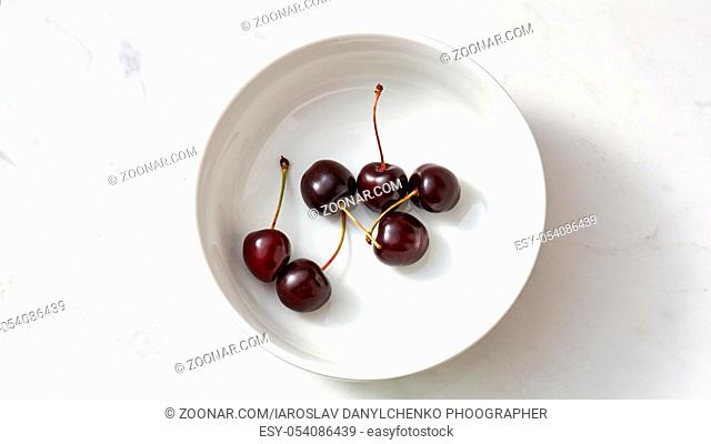 Ripe sweet cherry in the white plate on a gray background with copy space. Concept of clean organic eating. Flat lay