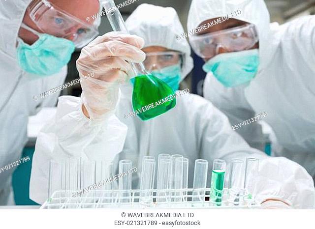 Chemist mixing green liquid in beaker with two chemists watching in the lab