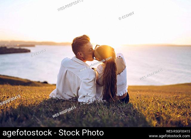 Young couple kissing while relaxing on hill at Mirador de La Providencia, Gijon, Spain