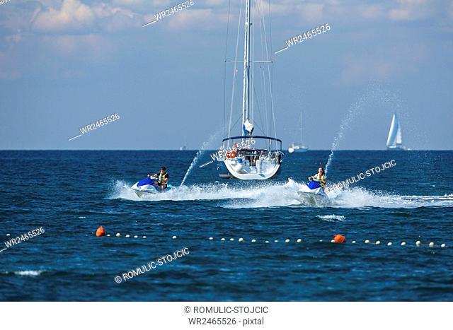 Jet boats racing at high speed next to sailboat