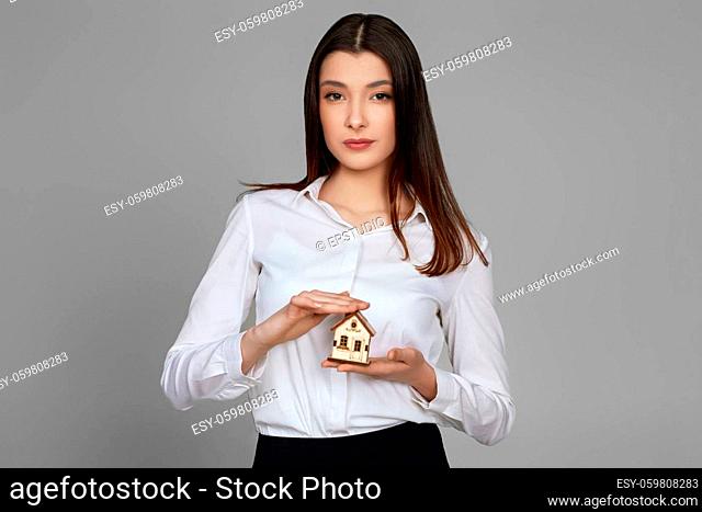 beautiful woman holding little house on gray background. real estate insurance concept